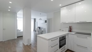 Une cuisine moderne avec des meubles blancs, un four encastré et un coin repas comprenant une table et des chaises.