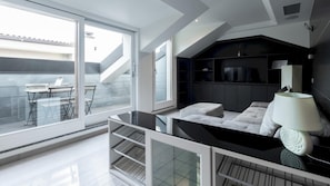 A modern bedroom with a large window, a sofa, a TV, and a lamp.