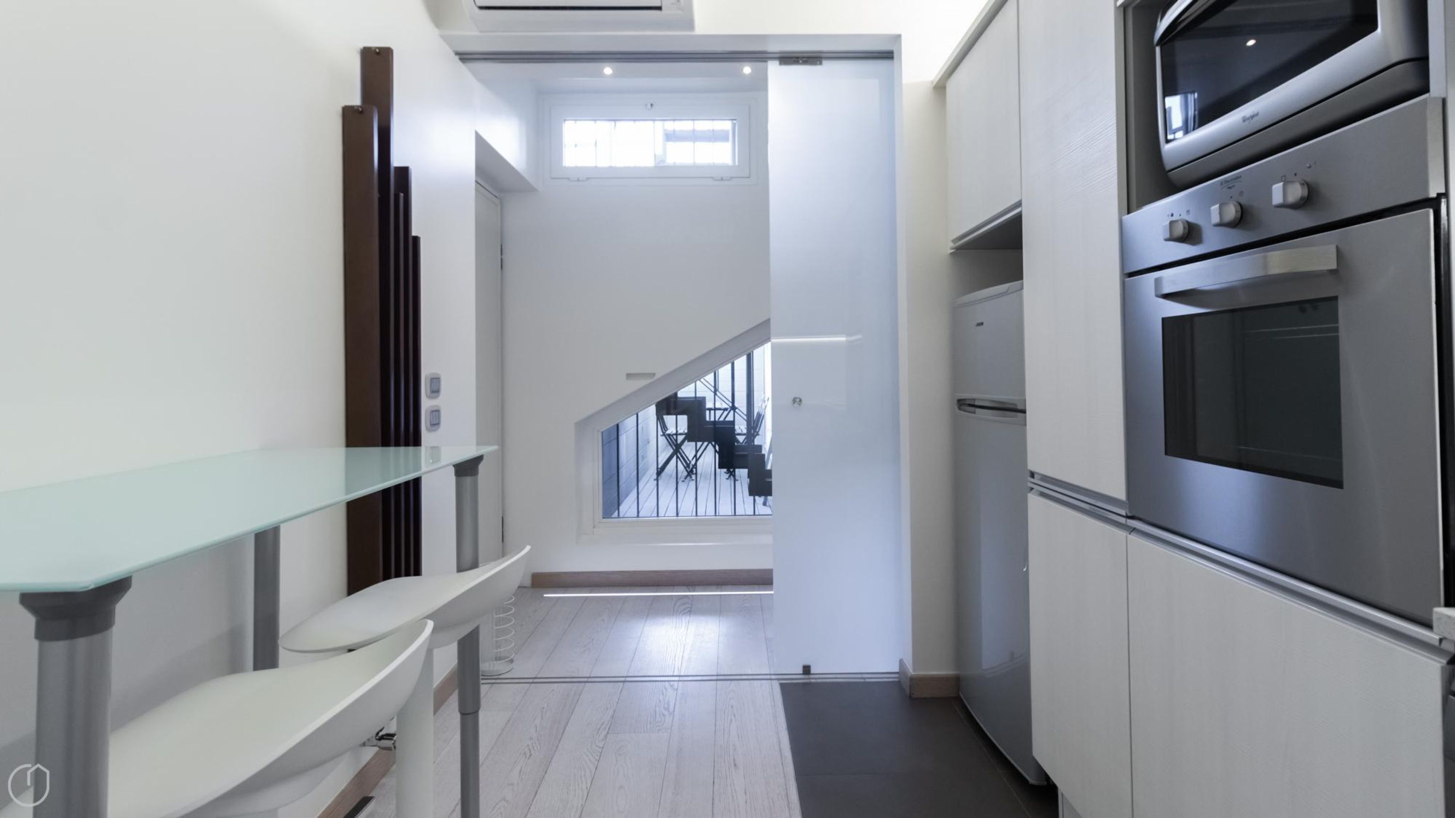 A modern kitchen with stainless steel appliances, a glass shelf, and a staircase leading to a balcony.