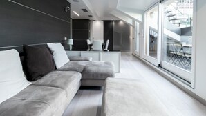 A modern living room with a grey sectional sofa, a white coffee table, and a glass door leading to a balcony with outdoor furniture. - Italianway Collection - Corso Venezia 7 - Traviata (Milan)