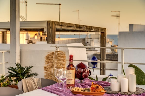 A dining table with a bottle of wine, glasses, a plate of food, and candles on a balcony overlooking a marina.