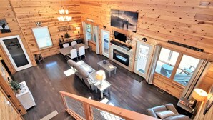 A wooden cabin interior with a dining area, sofa, fireplace, and large windows. - Panoramic Views, LED Hot Tub, King Suite, Wi-Fi, Minutes to Downtown Gatlinburg (Gatlinburg)