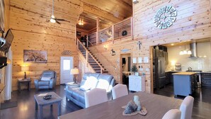 A cozy log cabin interior with a living room, dining area, kitchen, and a staircase leading to an upper level. - Panoramic Views, LED Hot Tub, King Suite, Wi-Fi, Minutes to Downtown Gatlinburg (Gatlinburg)