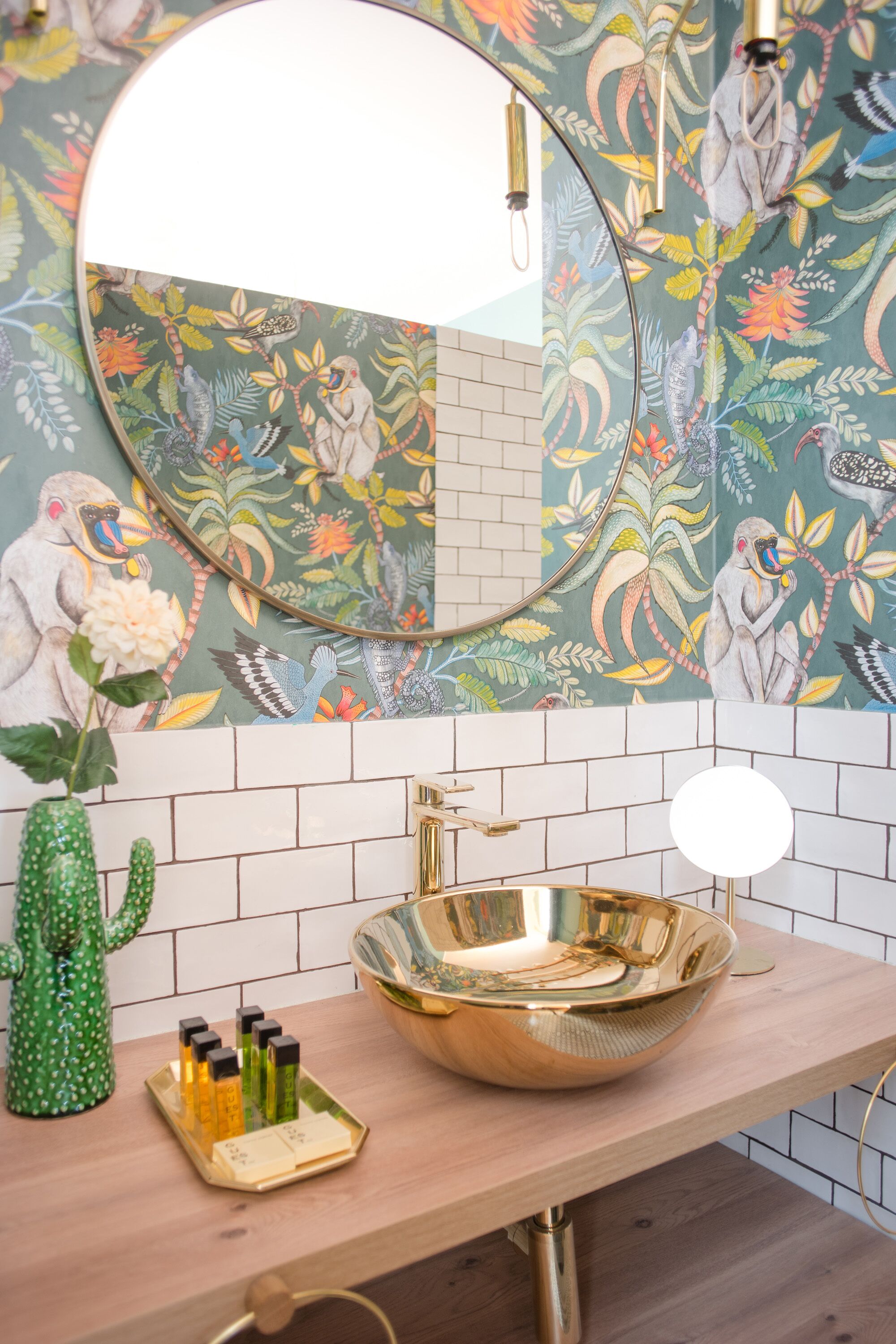 A bathroom with a round mirror, a gold sink, and a floral wall mural.