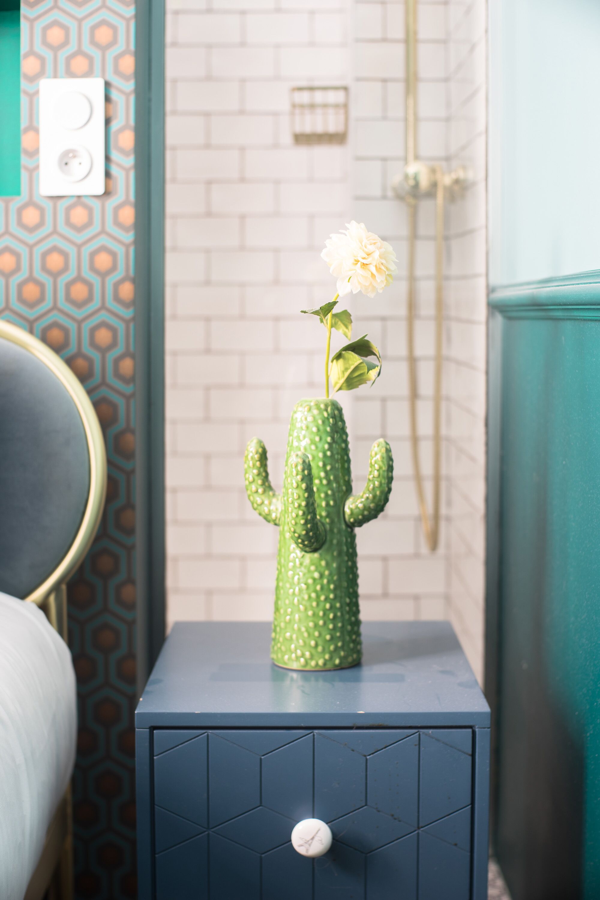 Un cactus con una flor sobre un mueble azul oscuro en una habitación con papel tapiz estampado y pared de ladrillo blanco.