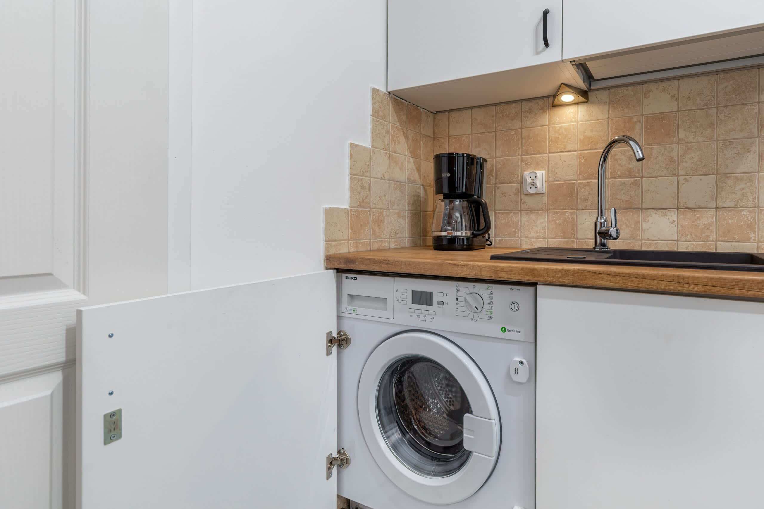 A compact kitchen with a washing machine, a coffee maker, and a sink.
