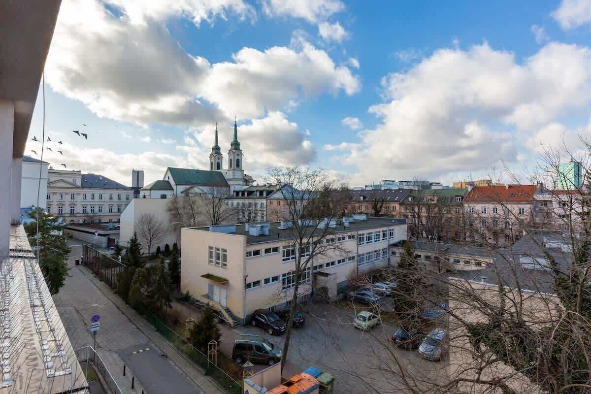 Une vue sur un paysage urbain avec une église imposante à deux flèches, entourée d’immeubles et de voitures garées.