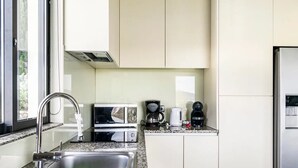 Eine moderne Küche mit Spüle aus Edelstahl, einer Mikrowelle, einer Kaffeemaschine und einem Kühlschrank.