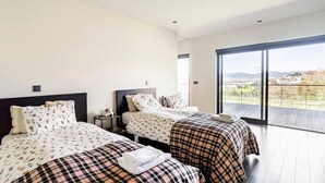Ein modernes Schlafzimmer mit zwei Betten, einem Balkon und Blick auf die Stadt.