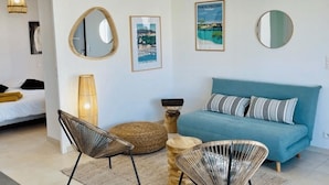 Uma sala de estar moderna com um sofá azul, cadeiras de vime, uma mesa redonda pequena e espelhos fixados na parede.