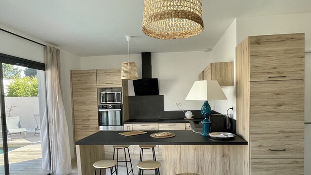 Uma cozinha moderna com ilha central, banquetas, luminária pendente e vista para o exterior.