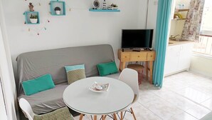 Ett modernt vardagsrum med en grå soffa, turkosa kuddar, ett runt vitt bord och en tv-apparat placerad på ett träställ.