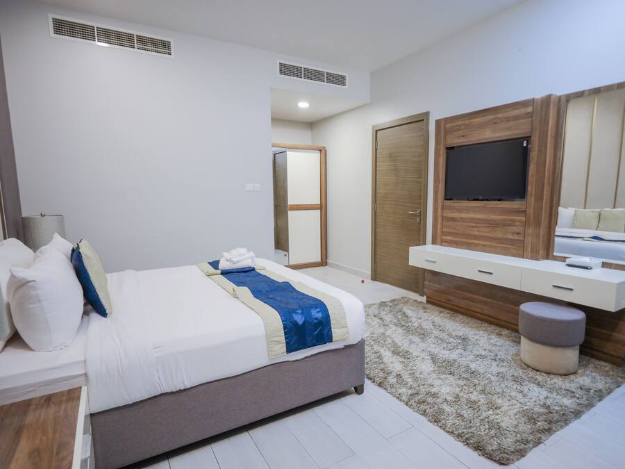 A modern bedroom with a bed, a TV mounted on a wooden panel, a bedside table, and a mirror.