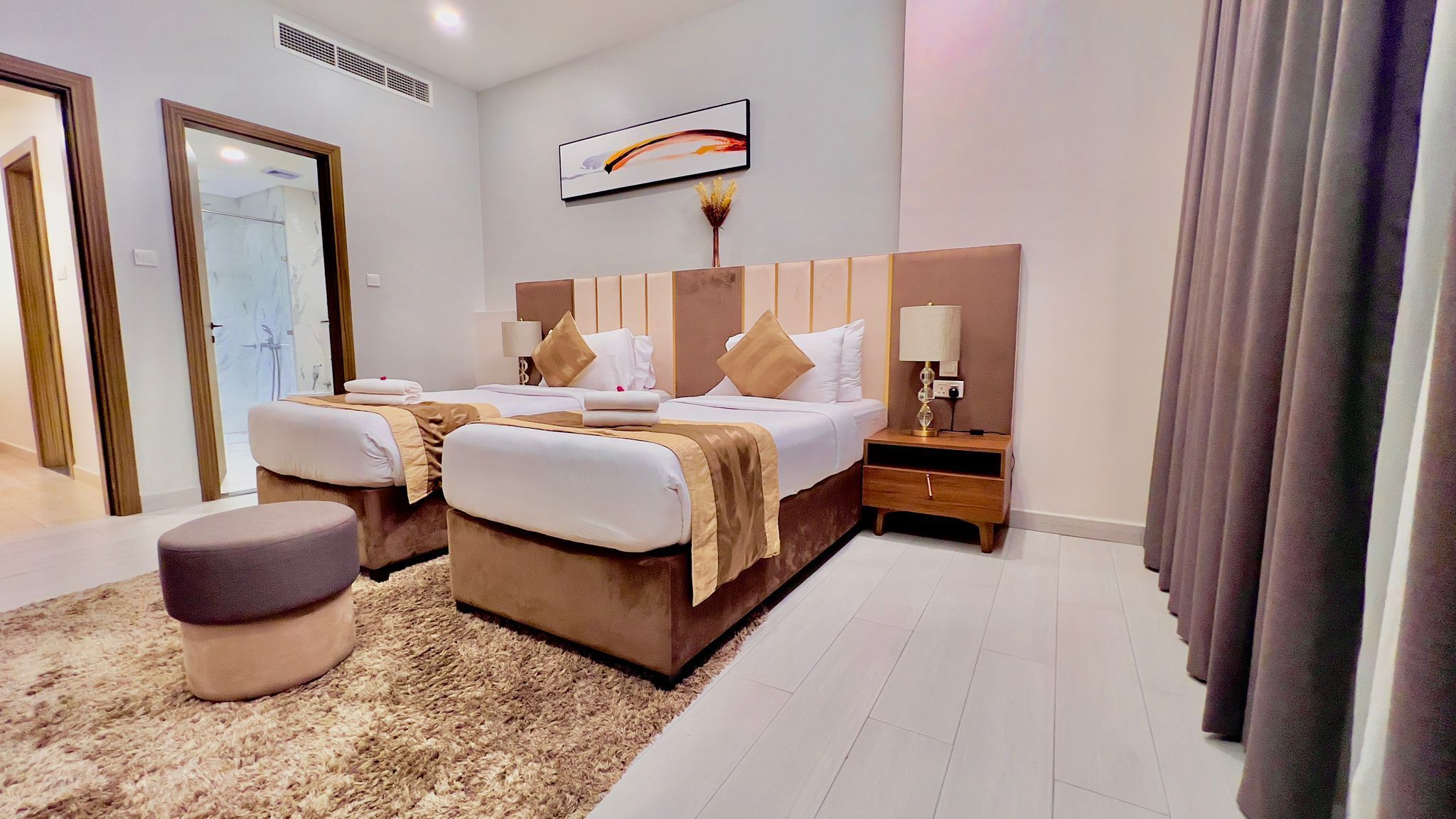 Una habitación de hotel moderna con dos camas, un ventanal grande, un cabecero de madera, una mesita de noche con lámpara y una alfombra mullida.