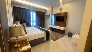 A modern hotel room with a large bed, a TV mounted on the wall, a small desk with a lamp, and a window with curtains. - BW Suites & Spa (Manama)
