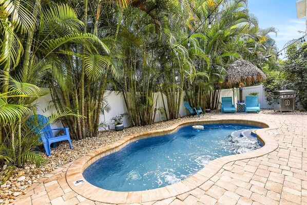 Une piscine entourée d’une végétation luxuriante et bordée d’une structure à toit de chaume.