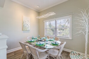 Un comedor con una mesa de vidrio, sillas de mimbre y una escultura de árbol blanco.