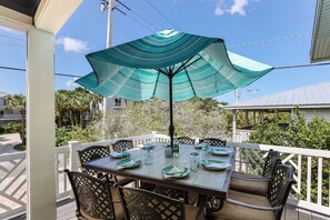 Un espace extérieur abrité, aménagé pour les repas, avec une table pour quatre personnes, entourée de chaises, et un parasol pour faire de l’ombre.