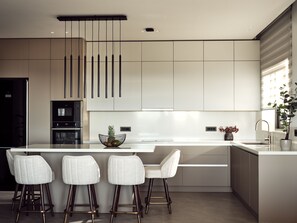 A modern kitchen with a central island, bar stools, and a built-in oven.