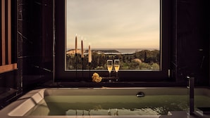 Uma banheira com velas e copos, uma janela com vista para a paisagem.