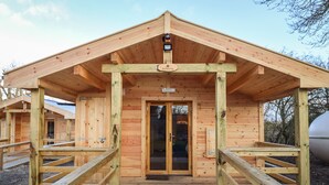 A wooden cabin with a covered entrance and a ramp leading to the door. - Buttercup Lodge (Leiston)