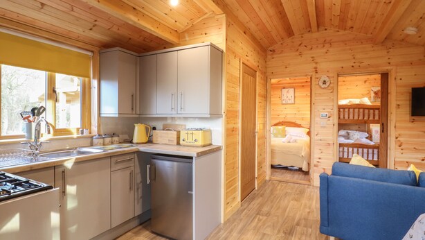 A compact wooden cabin with a kitchen, a dining area, and a bedroom. - Buttercup Lodge (Leiston)