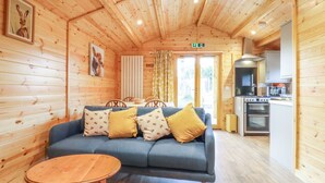 A cozy cabin interior with a blue sofa, wooden walls, a dining area, and a kitchenette. - Buttercup Lodge (Leiston)