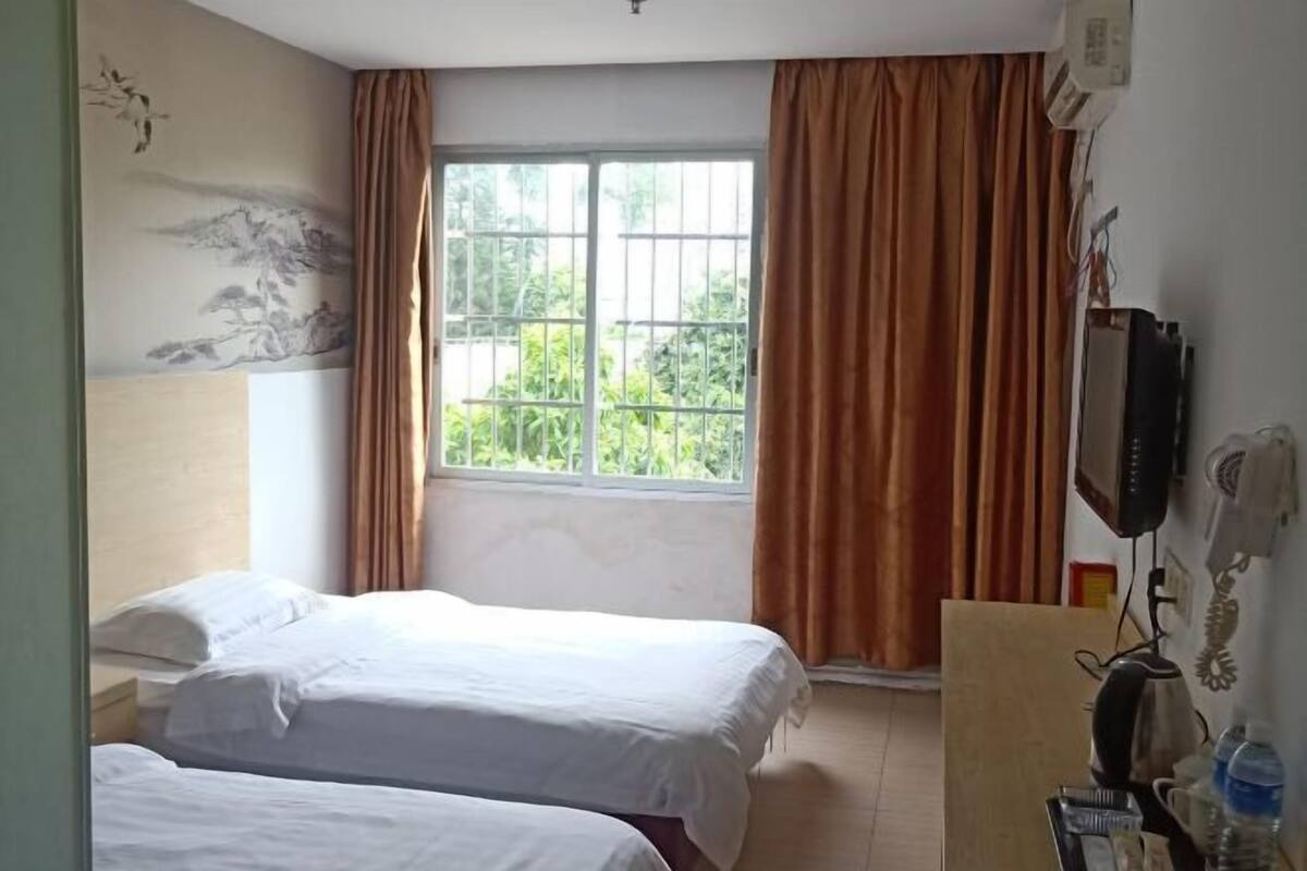 Ein Hotelzimmer mit zwei Betten, einem Vorhangfenster, einem an der Wand befestigten Telefon und einem Gemälde.