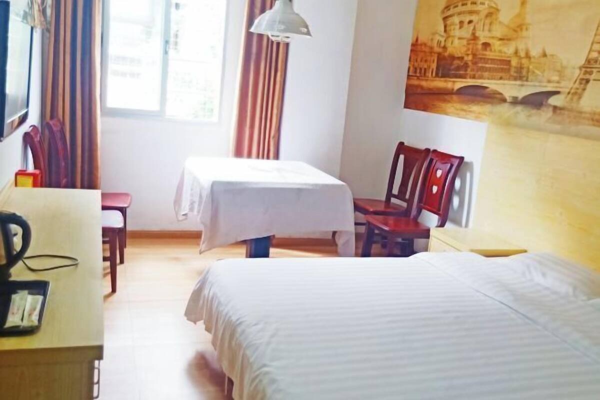 Ein Hotelzimmer mit einem Bett, einem Schreibtisch mit Stuhl, einem Tisch mit Stuhl, einer Lampe und einem großen Gemälde einer Brücke.