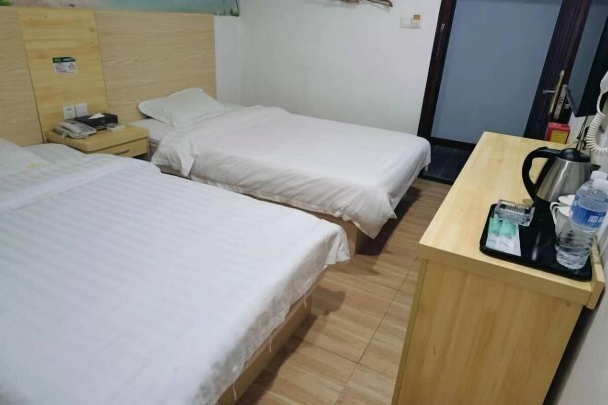 Ein Hotelzimmer mit zwei Einzelbetten, einem Holztisch mit Wasserkocher, Telefon und einer Wasserflasche.