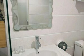 Casa de banho com lavatório branco, espelho e sanita.