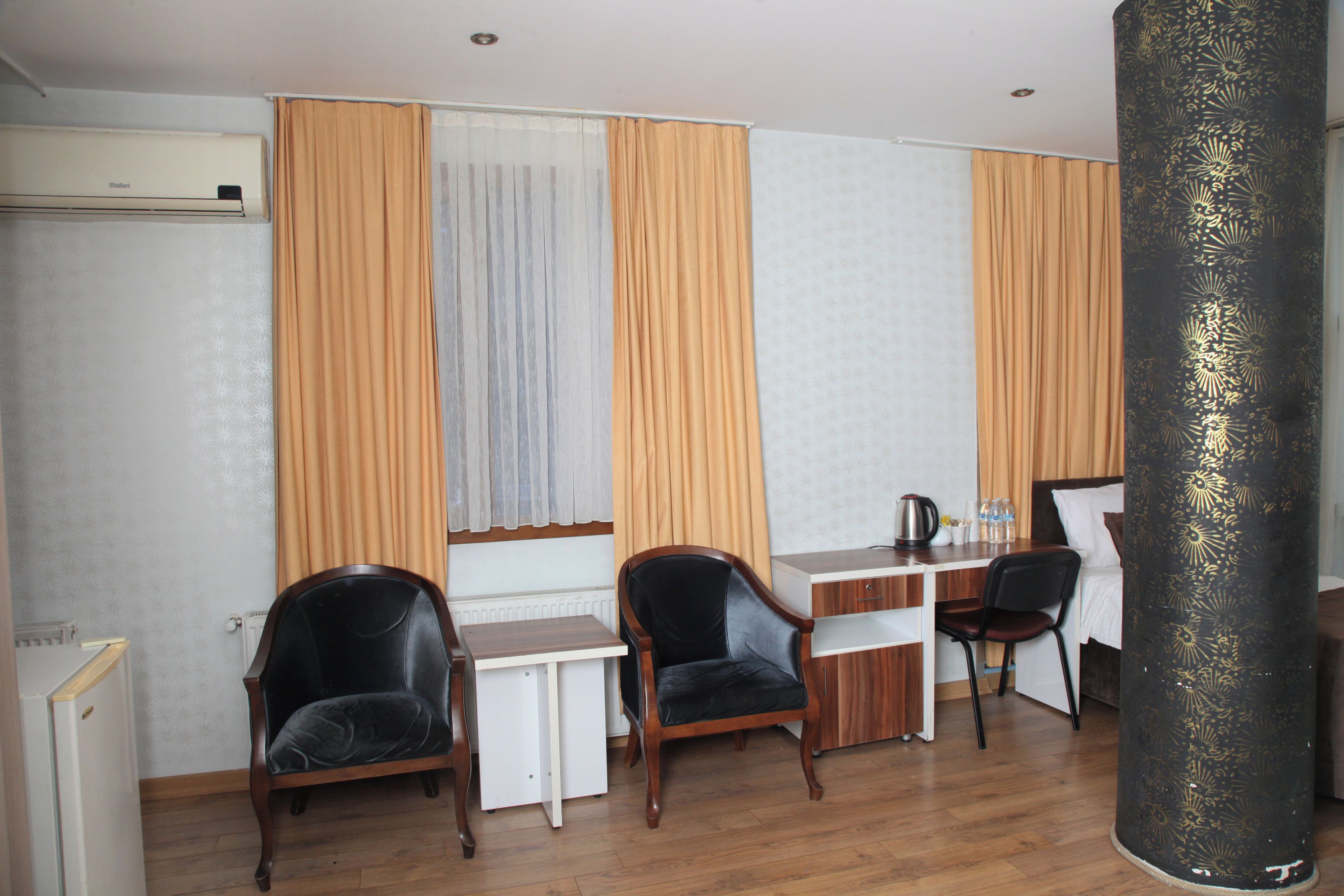 A hotel room with a wooden desk, two chairs, a bed, and a large pillar.