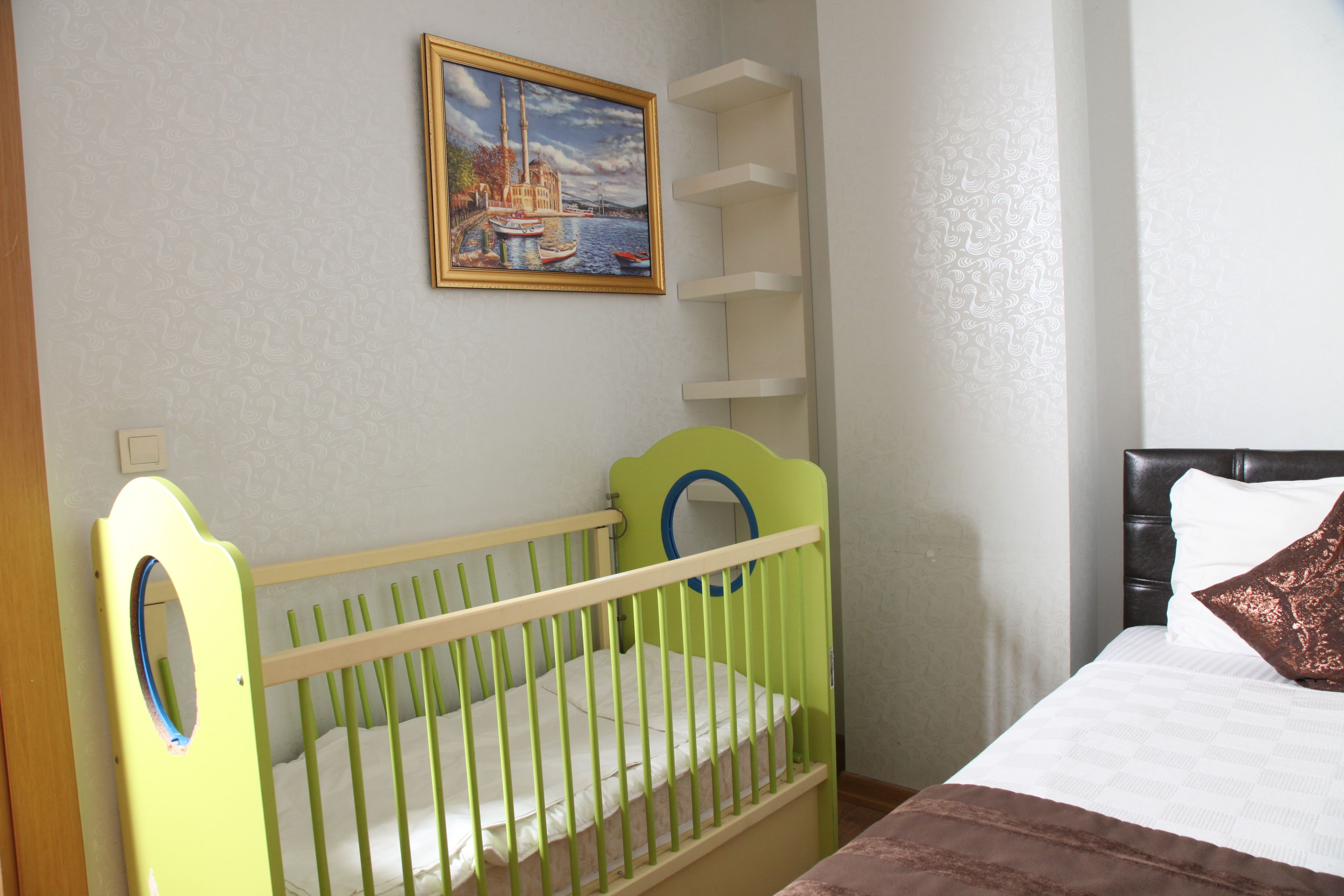 Una habitación con una cuna, una cama, un cuadro en la pared y una estantería.