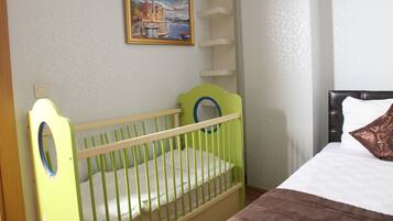 Una habitación con una cuna, una cama, un cuadro en la pared y una estantería.