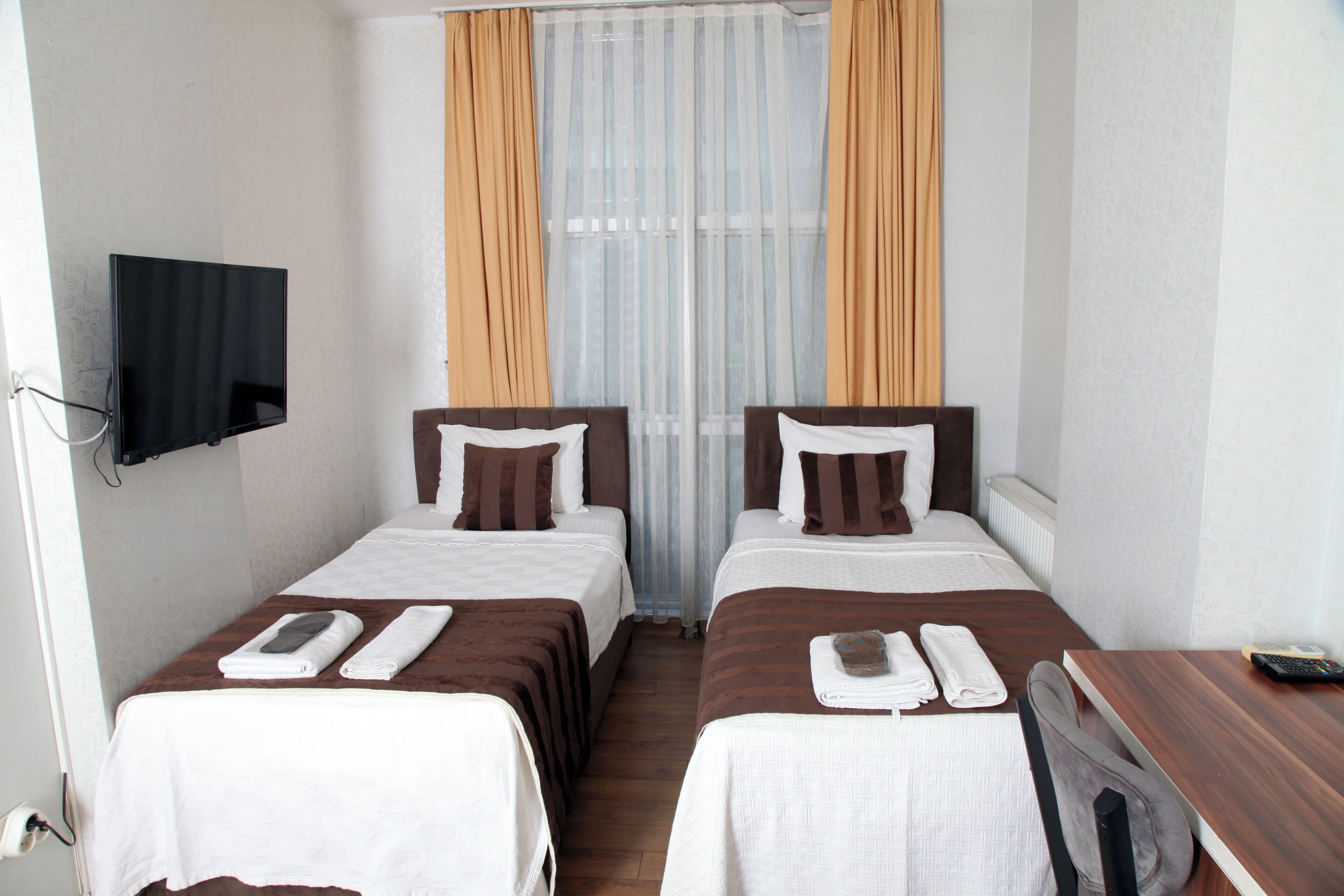 A hotel room with two beds, a TV, a desk, and a window with curtains.