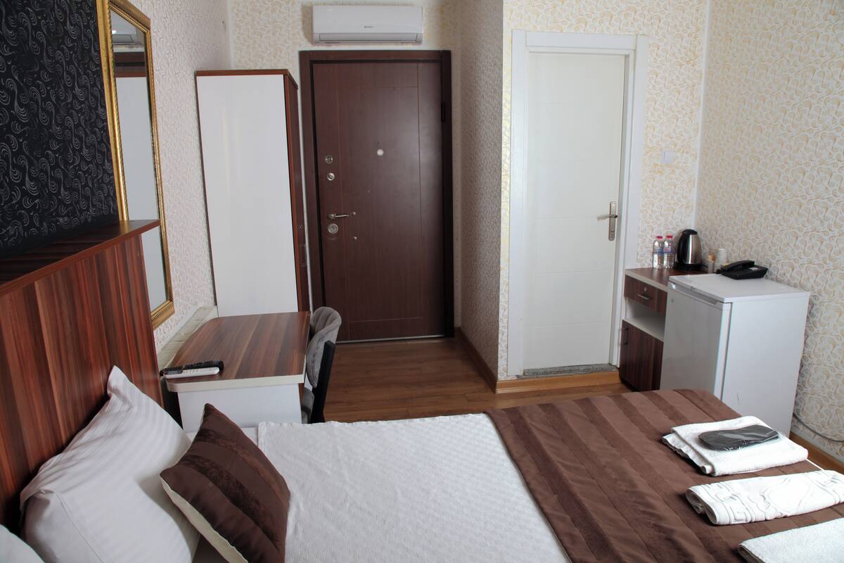 A hotel room with a bed, a desk, a wardrobe, a door, and a small kitchenette.