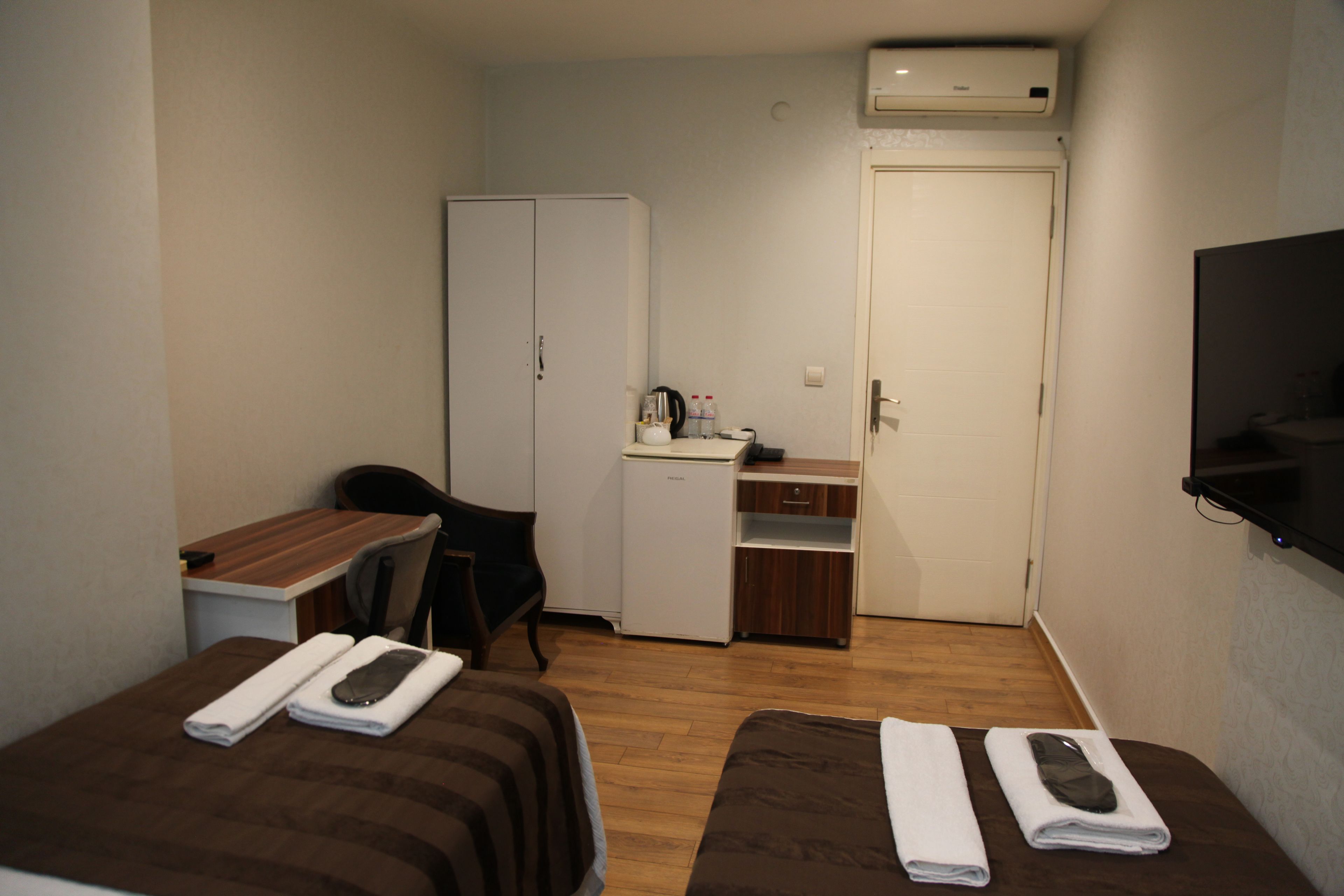 Habitación de hotel con dos camas, un escritorio, una silla, armario, kitchenette pequeño y televisor.