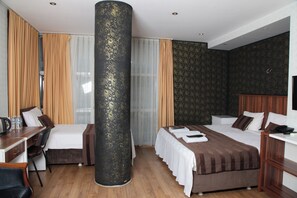 A hotel room with a large cylindrical pillar, two beds, a desk, and a chair. - Garden Hill Hotel (Istanbul)