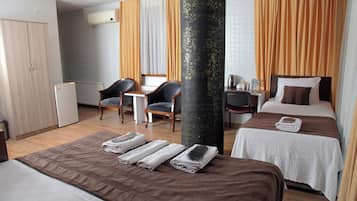 A hotel room with two beds, a desk, a chair, a wardrobe, and a large pillar.
