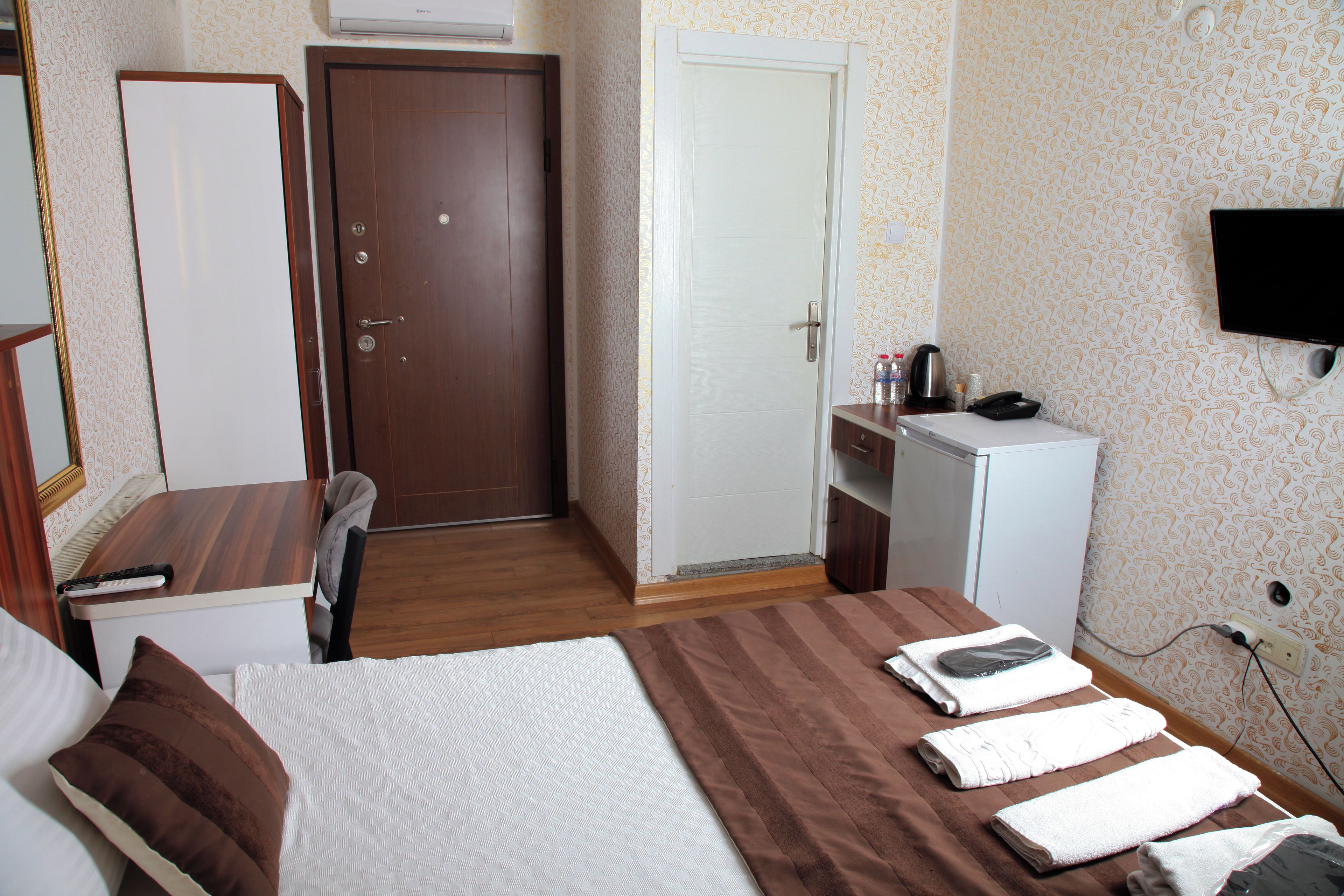 A hotel room with a bed, a desk, a chair, a wardrobe, a television, and a small kitchenette.