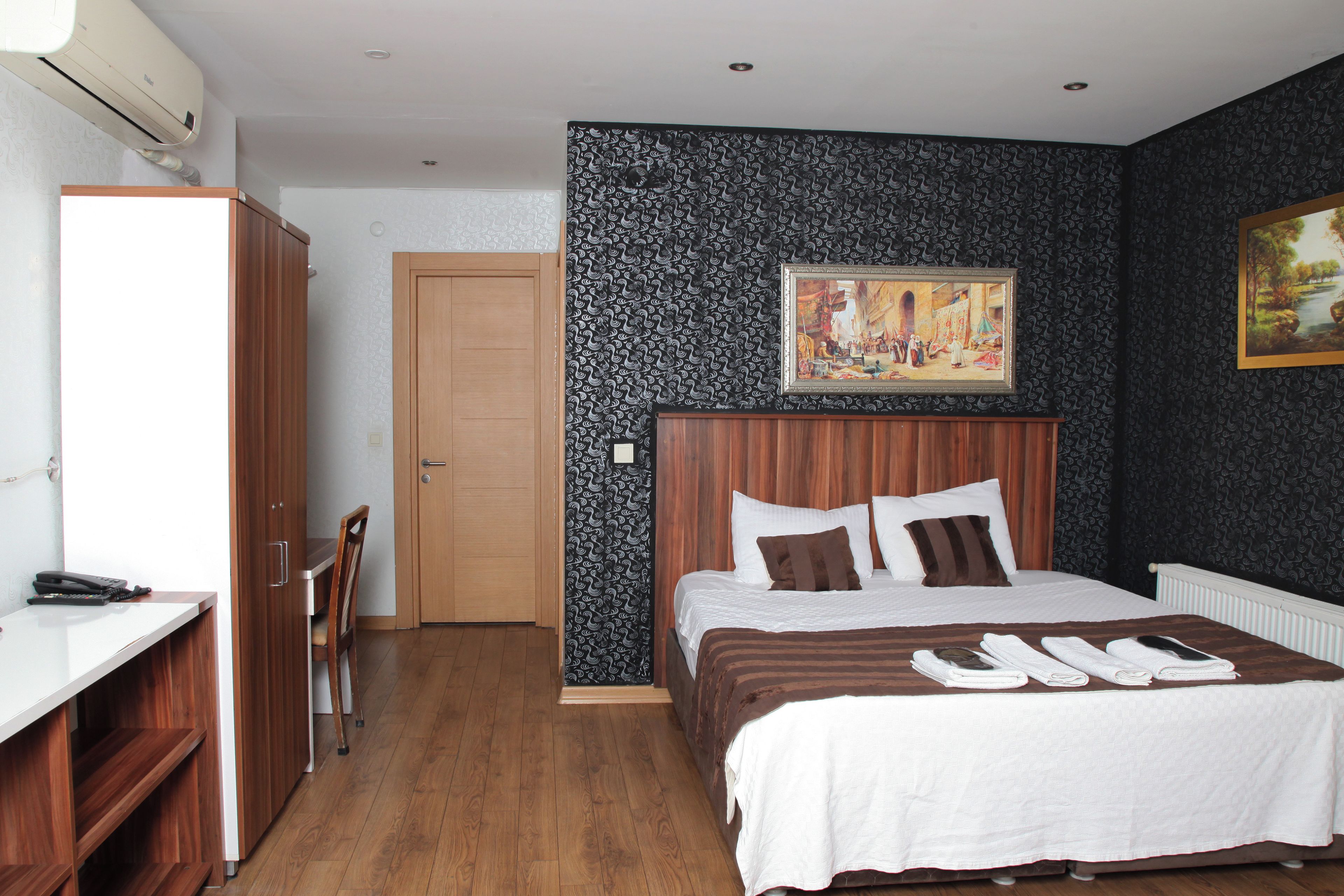 Una habitación de hotel con cama, escritorio, silla, armario y un cuadro en la pared.
