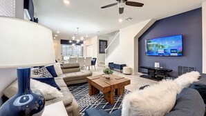 A modern living room with a ceiling fan, a TV mounted on the wall, and a dining area in the background. - 5⭐ Solterra Villa with Lake View • 20 Minutes to Disney (Davenport)