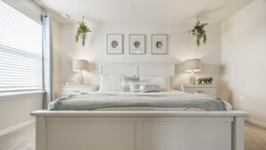 A bedroom with a large bed, two bedside tables, a window with blinds, and three framed pictures on the wall. - 5⭐ Solterra Villa with Lake View • 20 Minutes to Disney (Davenport)