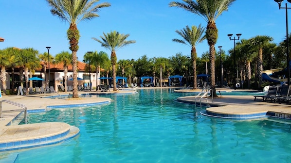 A pool area with palm trees, lounge chairs, and umbrellas.