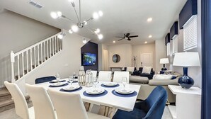 A dining area with a white table set for six, a ceiling fan, and a TV mounted on the wall. - 5⭐ Solterra Villa with Lake View • 20 Minutes to Disney (Davenport)