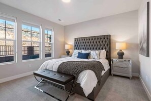 A bedroom with a large bed, two bedside tables with lamps, a bench, and a view of a desert landscape through the windows. - Casa De Pazos by RedAwning (Washington)