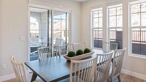 Un espace repas comprenant une table et des chaises, de grandes fenêtres et une vue sur l’extérieur.