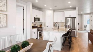 Une cuisine moderne avec des meubles blancs, des appareils en acier inoxydable et un îlot central doté de tabourets de bar.