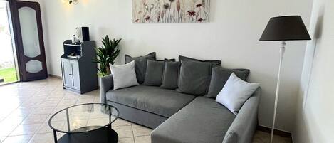 A modern living room with a grey sectional sofa, a glass coffee table, a floor lamp, and a painting on the wall.