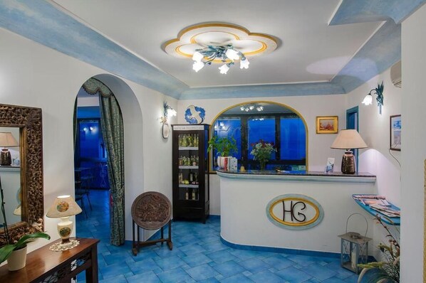 A reception area with a blue-tiled floor, a reception desk with a logo, a chandelier, and a view through a window.